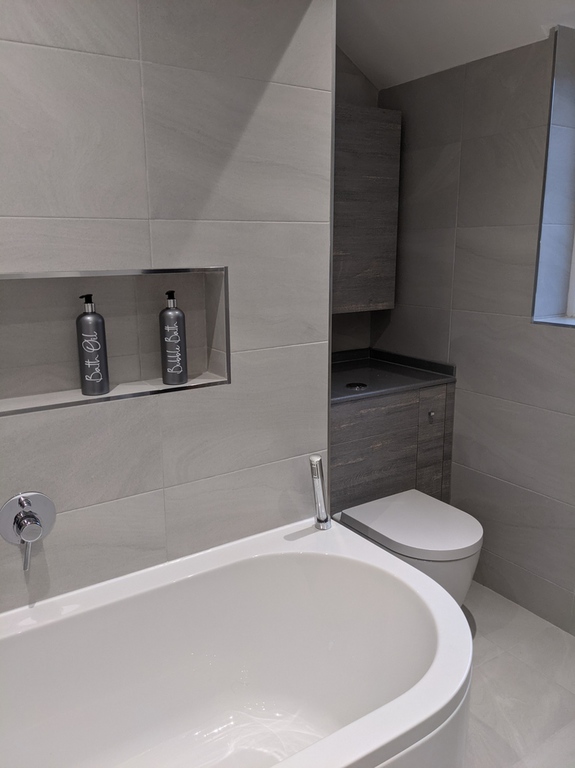 New bathroom, featuring tiled floor and walls, bath and toilet with an recessed shelf above the bath for soaps, shower gels and shampoo.