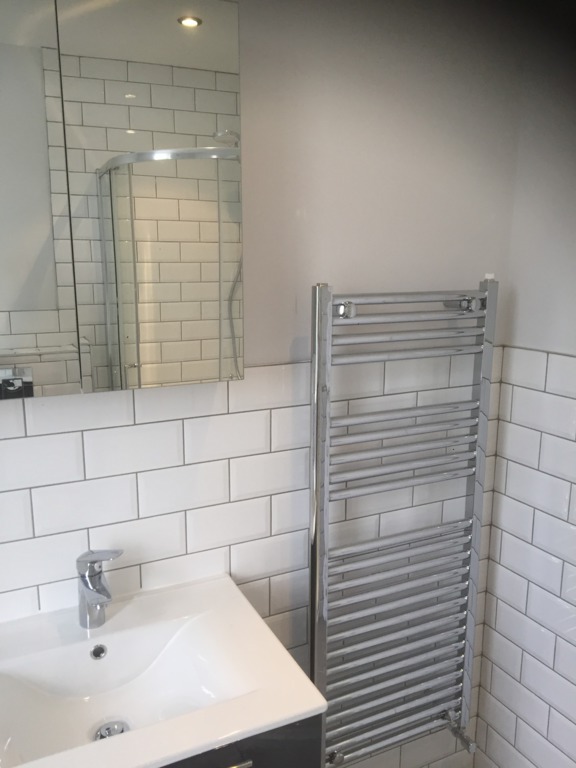 New bathroom, featuring part metro-tiled wall, white sink, chrome mixer tap, towel rail and mirrored bathroom cabinet