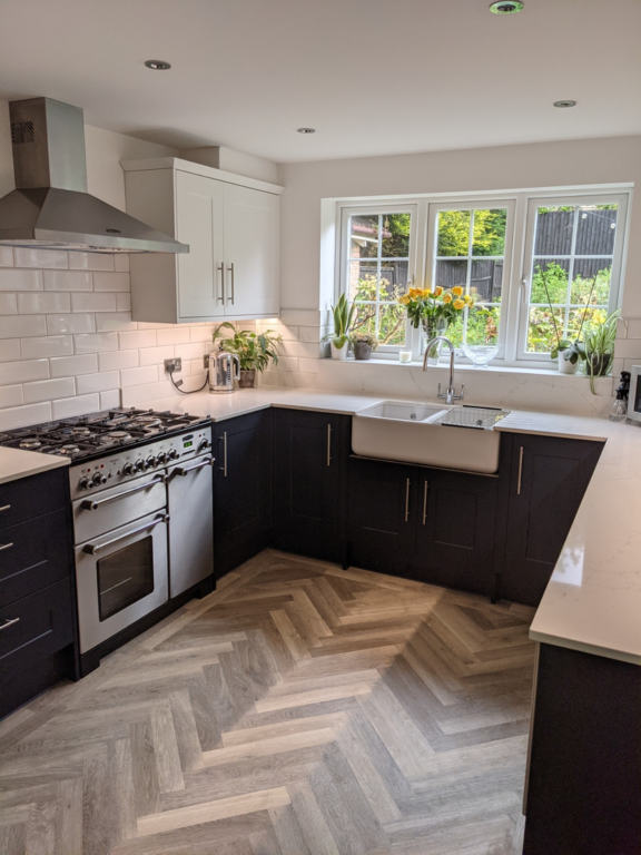 New dark blue kitchen (shaker-style), with a parquet-style wooden floor, marble worktops and a Butler sink below a main window, over looking a garden.