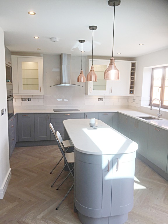 New grey kitchen (shaker-style), with island. Three brass lamps hang from the ceiling about the kitchen island, with a parquet-style wooden floor